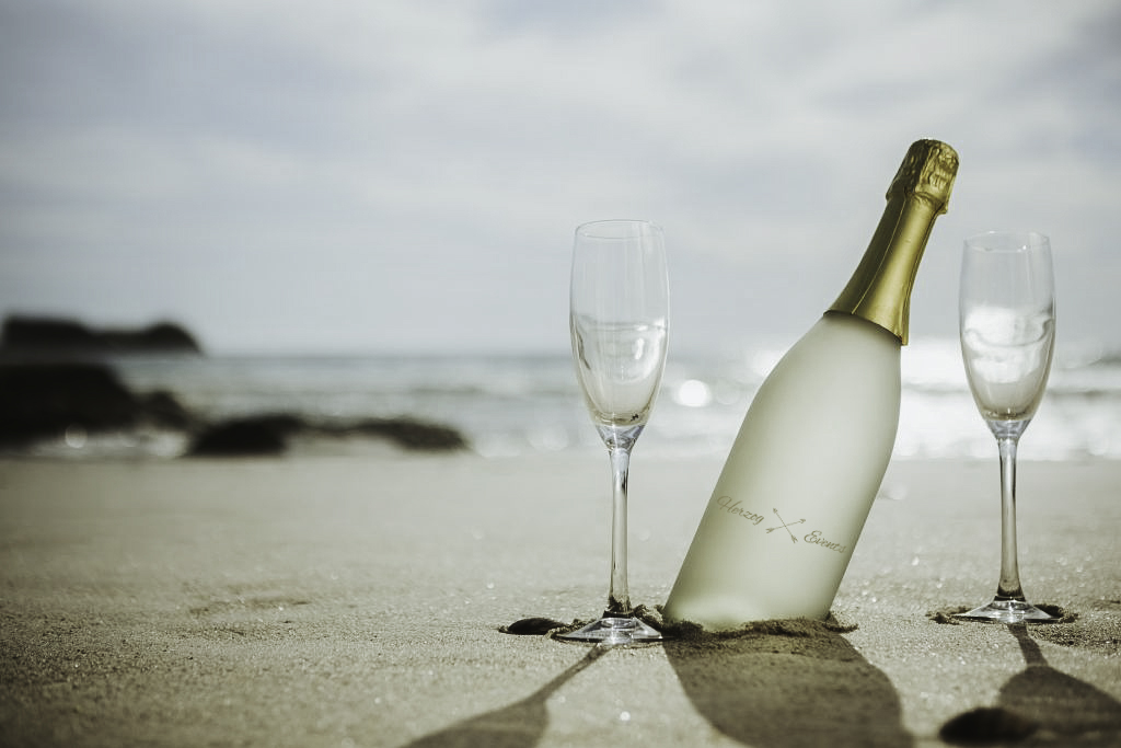 Sektflasche und zwei Gläser im Sand am Strand
